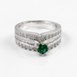 A silver-colored ring featuring a round green emerald-cut center stone and multiple rows of small clear baguette and round-cut stones along the band, shown on a clean white background.