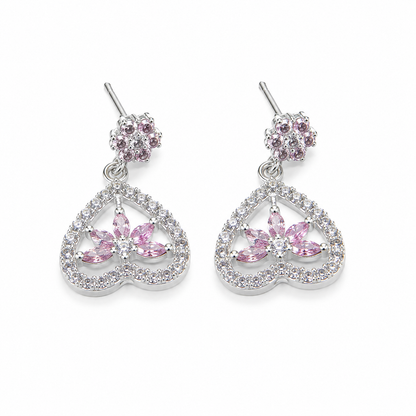 A pair of silver-toned dangle earrings featuring a small round cluster of pink stones at the top and a larger open heart-shaped drop with a central pink floral motif surrounded by clear stones, shown on a plain white background.