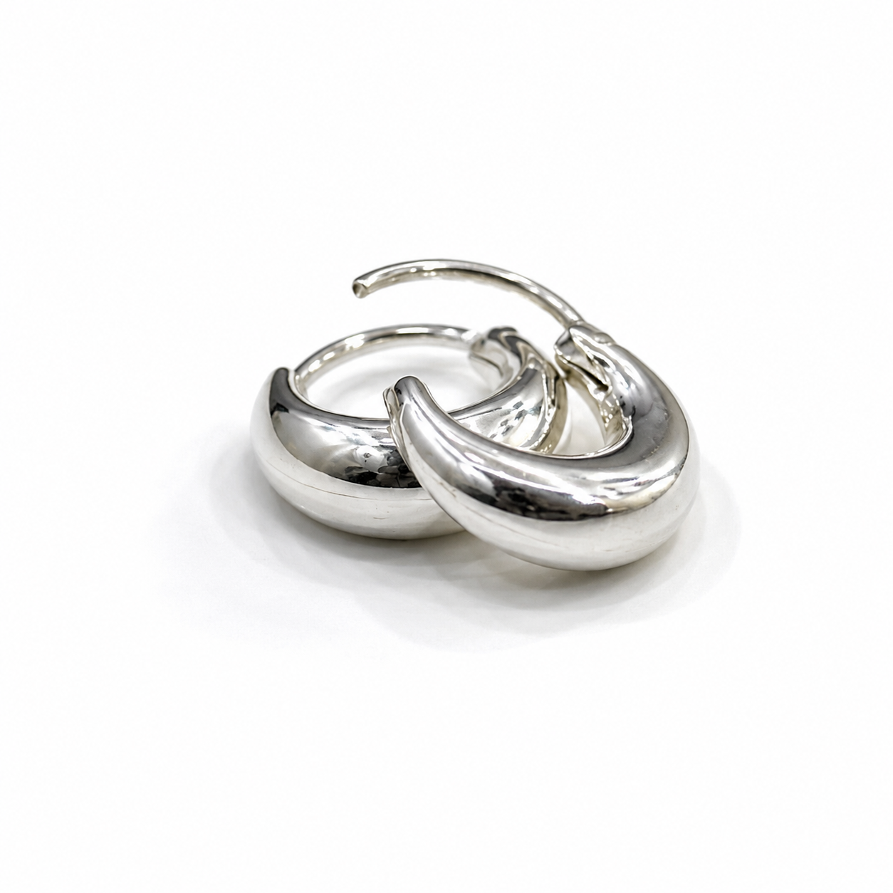 A pair of polished silver huggie hoop earrings with a smooth, curved, organic design, displayed on a clean white background.