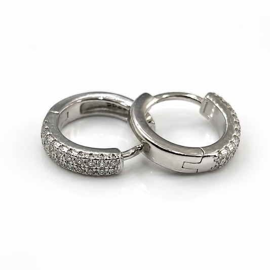 A pair of silver huggie hoop earrings embellished with pavé-set clear stones, displayed on a clean white background.
