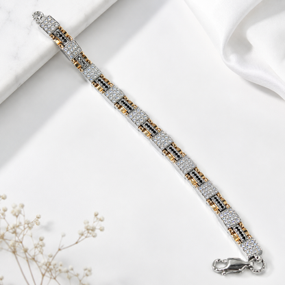 A silver-toned link bracelet with alternating rows of clear pavé stones and small gold and black accents, displayed diagonally on a white marble and satin background with dried flowers.