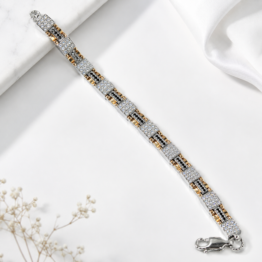 A silver-toned link bracelet with alternating rows of clear pavé stones and small gold and black accents, displayed diagonally on a white marble and satin background with dried flowers.