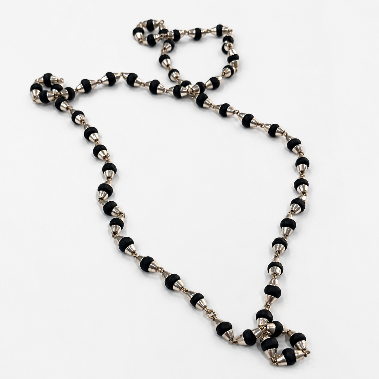 A beaded necklace featuring alternating black and silver metallic beads, arranged in a loose loop on a plain white background.