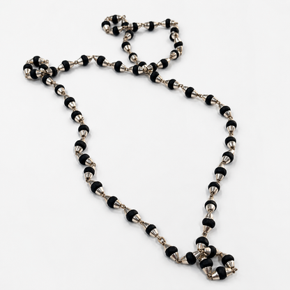 A beaded necklace featuring alternating black and silver metallic beads, arranged in a loose loop on a plain white background.