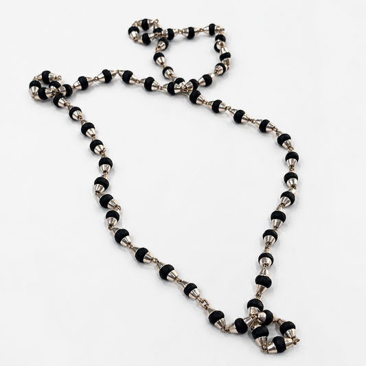 A beaded necklace featuring alternating black and silver metallic beads, arranged in a loose loop on a plain white background.