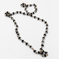A beaded necklace featuring alternating black and silver metallic beads, arranged in a loose loop on a plain white background.